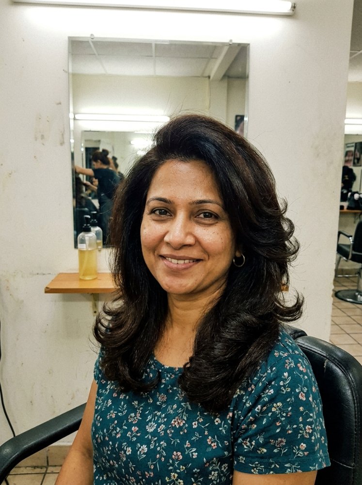 dark brown subtle dimension featuring The hair is dark brown with subtle dimension, featuring loose, flowing curls that frame the face. It appears to be shoulder-length or longer, with layers that enhance its movement and texture, and has a healthy, glossy appearance. The cut style is layered, adding volume and flow to the overall look