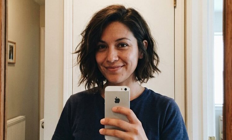 The hair is dark brown with a subtle, natural texture and a medium length that falls just above the shoulders. It has a relaxed, wavy cut with layers that add movement and a face-framing style that enhances the overall shape. The hair appears to have a subtle dimension, but obvious dimensional color are visible, and there is evidence of curls, braids or gray blending, with minimal regrowth visible