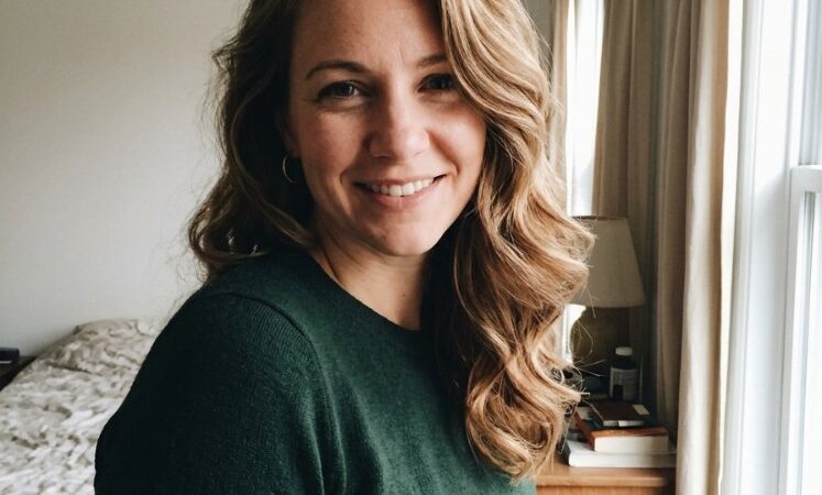 The hair visible in this is a medium to long length with a wavy texture. It appears to be a multi-dimensional blonde color with subtle highlights and lowlights, possibly achieved through balayage, and has a natural-looking, glossy finish, suggesting the use of a toner or gloss. The cut style features layers that enhance the hair's movement and flow, with face-framing elements that add to its dimension
